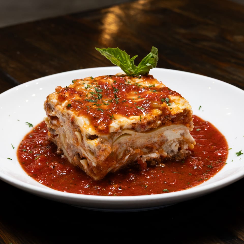A generous slice of lasagna with rich red sauce and fresh basil on a white plate.