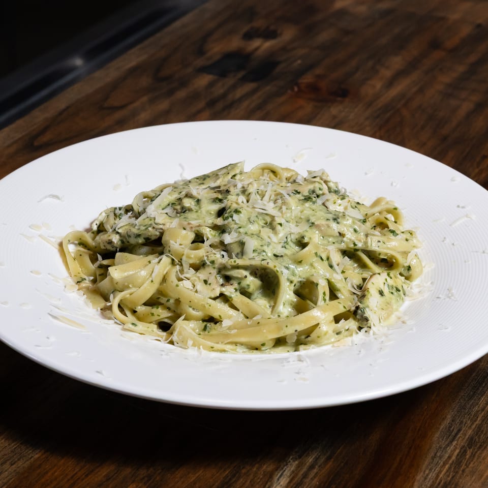 Fettuccine pasta with creamy pesto sauce and grated Parmesan cheese on a white plate.